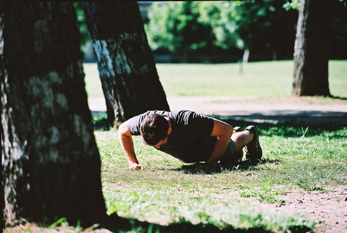 Person doing push-ups on grass in public park