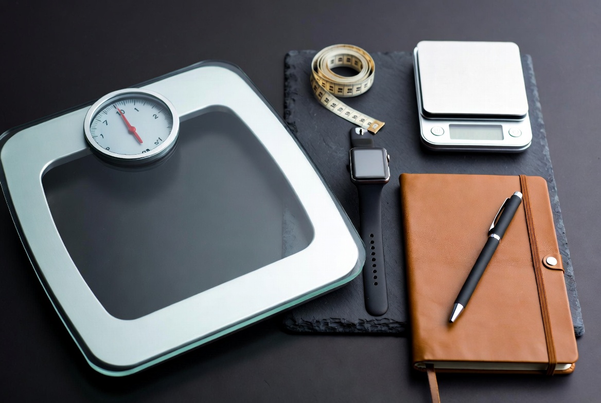 Flat lay of weight loss tools - scale, tape, food scale, watch, journal